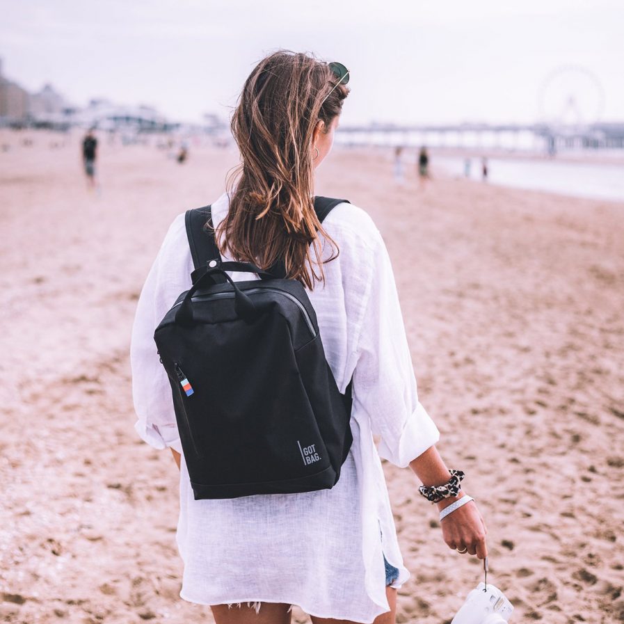 Frau am Strand mit schwarzem Rucksack